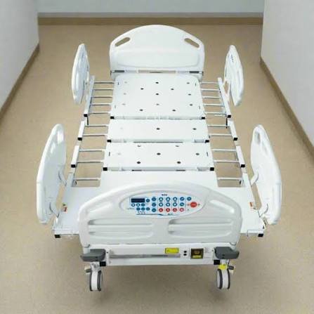 A fully electric 5-function ICU bed with integrated plastic side rails and an emergency mechanical CPR release handle next to a standard manual hospital patient bed