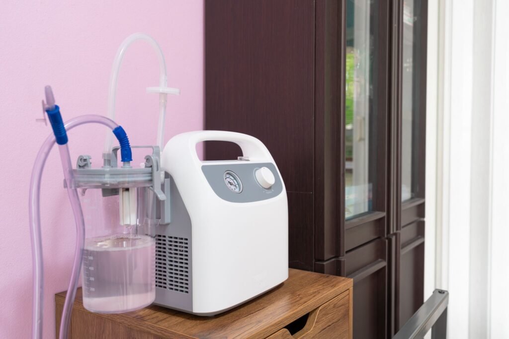 Portable medical phlegm suction machine setup with a clear collection jar, pressure regulator dial, and silicone tubes for home patient care